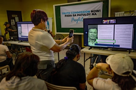 A woman takes a picture of a screen showing Rodrigo Duterte and documents.