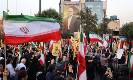 حشد من الناس، بعضهم يحمل العلم الإيراني. صورة كبيرة لإسماعيل هنية معروضة على جانب أحد المباني