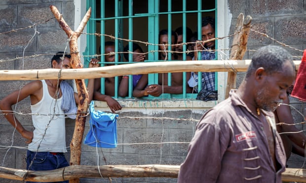 Prisoners look out at Adamo Anshebo, right, who is being held as an alleged kingpin, as he walks through the detention centre in Metema. He denies trafficking charges.