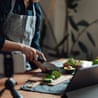 A person making a recipe while looking at a tablet and taking a video on their phone