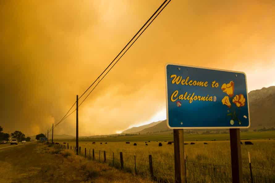 The Markleeville sign welcomes people to California as the smoke from the Tamarack fire rises in the background.