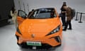 visitors pore over an orange MG 4 EV electric sports car on display at the Beijing Auto Show.