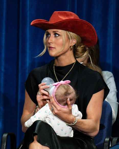 A woman wearing a cowboy hat feeds her baby with a bottle while sitting on stage