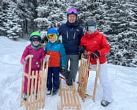 Family in skiwear standing with wooden sledges on snow