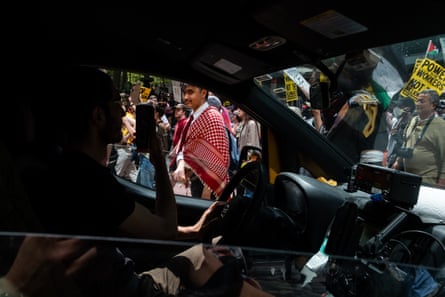 person in car holds up phone to film people holding signs and flags outside