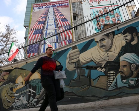An Iranian man walks next to a wall painting of Iranian soldiers (down) nearby an anti-US and Israel billboard in Tehran, Iran on 29 January 2026.