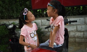 Two sisters play on their parents’ electric scooter in Beijing.