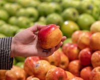 An apple is held aloft amid a selection of red and green apples at a supermarket
