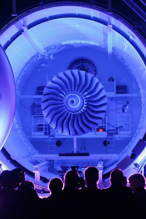 Visitors stand in front of the illuminated interior of a vacuum chamber for engine tests at a Rolls-Royce test centre.