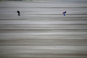 People walk on a windswept beach next to the course as high winds suspend play.