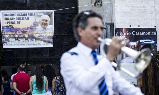 A man plays a trumpet in front of a banner showing Vittorio Casamonica and reading 'You conquered Rome, now you'll conquer paradise'.