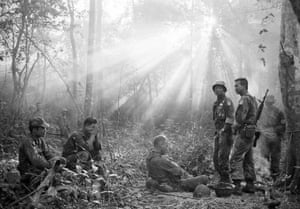 Sunlight breaks through dense foliage around the town of Binh Gia as South Vietnamese troops, joined by U.S. advisers, rest after a cold, damp, and tense night of waiting in an ambush position for a Viet Cong attack that did not come, January 1965