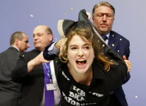 Security officers detain a protester who jumped on the table in front of the European Central Bank President Mario Draghi during a news conference in Frankfurt, April 15, 2015. The news conference was disrupted on Wednesday when a woman in a black T-shirt jumped on the podium. REUTERS/Kai Pfaffenbach