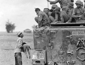 A distraught father holds the body of his child as South Vietnamese Rangers look down from their armoured vehicle, March 19, 1964