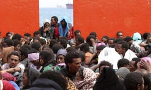 Migrants wait aboard an Italian navy ship to disembark in the Sicilian port of Augusta