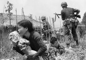 Under sniper fire, a Vietnamese woman carries a child to safety as Marines storm the village of My Son, near Da Nang, searching for Viet Cong insurgents, April 25, 1965. As was typical in such situations, the men of the village had mostly disappeared, and the remaining villagers revealed little when questioned by the Marines