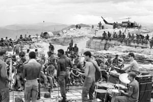 GIs of the 3rd Brigade, 101st Airborne Division, launch into a rock session while surrounded by symbols of the war: wooden bunkers, helicopter, and sandbags, July 1970