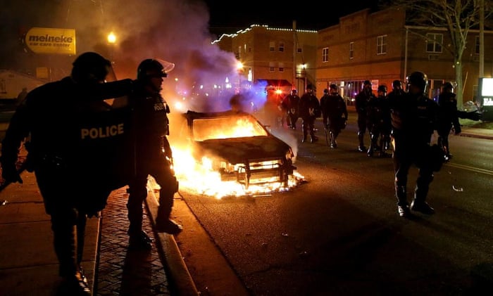 Police officers walk by a burning police car in Ferguson