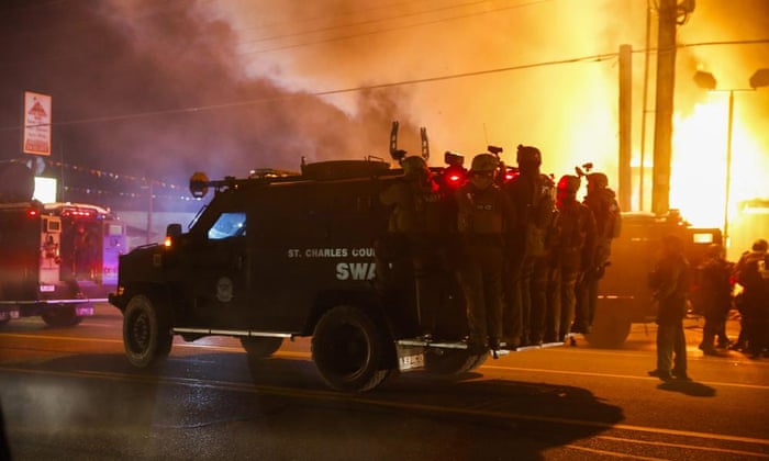 Police ride on a vehicle past a burning building that was set ablaze by protestors in Ferguson