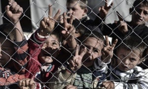 Young Syrian Kurdish boys make the 'V for victory' sign behind a fence at a refugee camp