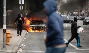 People walk past burning cars near the intersection of Pennsylvania Avenue and North Avenue