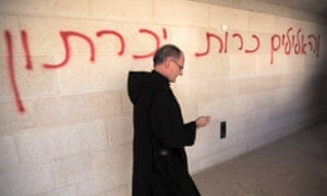 A priest walks past graffiti reading in Hebrew 'idols will be cast out' at the damaged Church of the Multiplication.