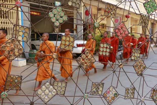 Monks collect morning alms outside the Maek Maek gallery, in front of sculpture by Battambang artist Mao Soviet.