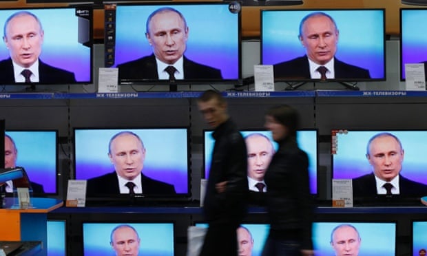 Muscovites walk past TV sets during Russian President Vladimir Putin’s annual nationwide phone-in.