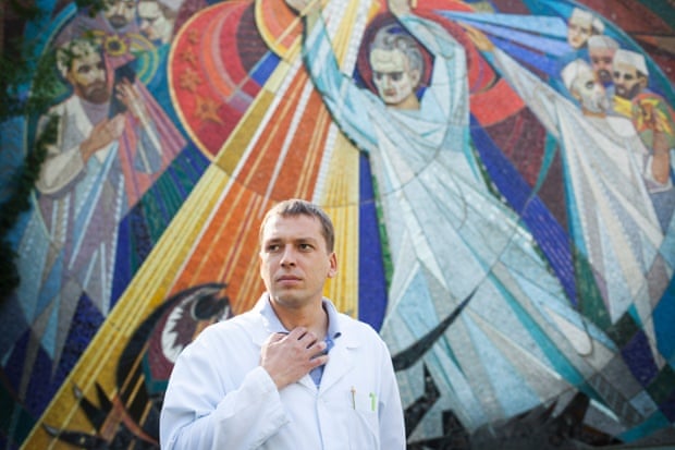 Andrei Semivolos stands outside the institute, in front of a Soviet mural depicting doctors fighting cancer. Photo by Joel van Houdt longread ukraine