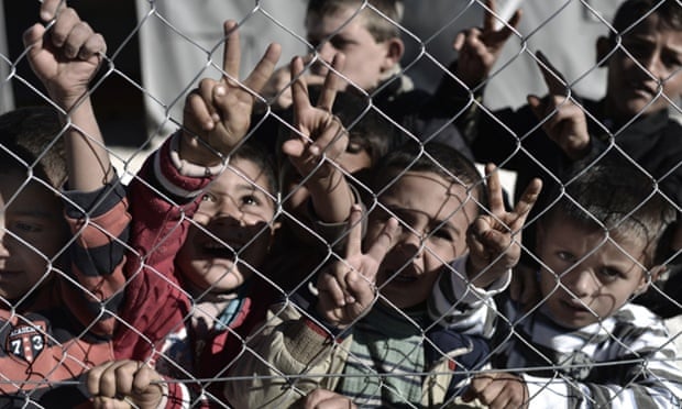 Young Syrian Kurdish boys make the 'V for victory' sign behind a fence at a refugee camp