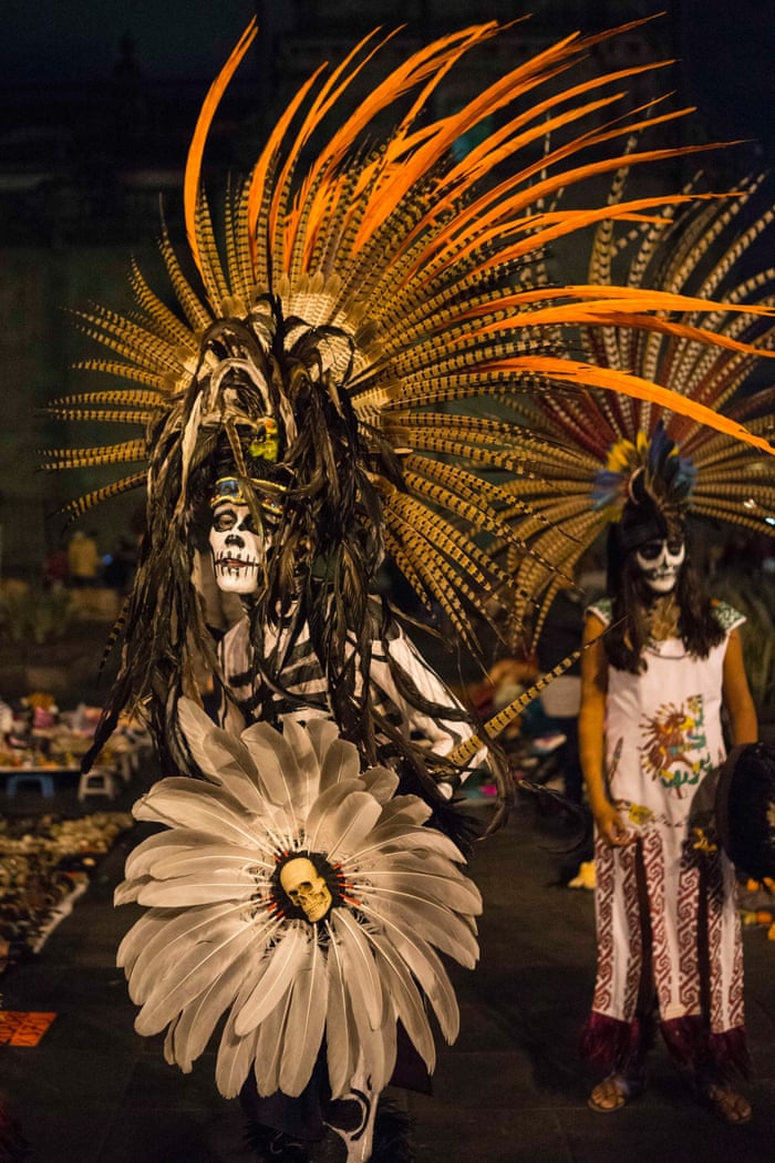A man wears an elaborate Day of the Dead costume made from feathers and skulls