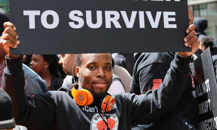 Activist with sign emphasizing the need for economic justice to ensure survival during march and rally on Manhattan's Upper West Side. -- #Fight for 15, an organization dedicated to raising the federal minimum wage, was joined by the Service Employees International Union and other labor activists as they march along Amsterdam Ave before staging a die in in front of a nearby McDonald's.