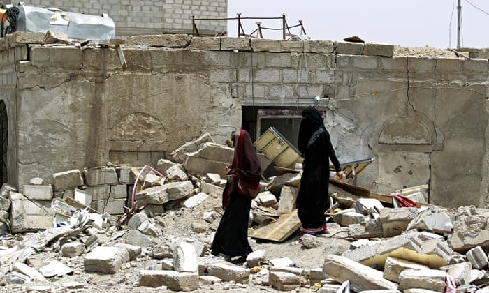 Yemeni women walk amid rubble of houses