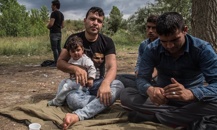 Yama Nayab with his daughter and other migrants in a makeshift camp in the fields and brush of an abandoned brick factory in the outskirts of Subotica, Serbia.