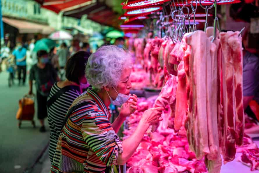 A woman removes her mask to smell the meat at a farmer’s market