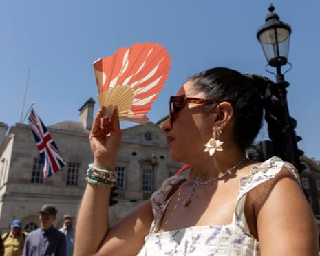 A person shields their face from the heat of the sun with a fan, in central London.