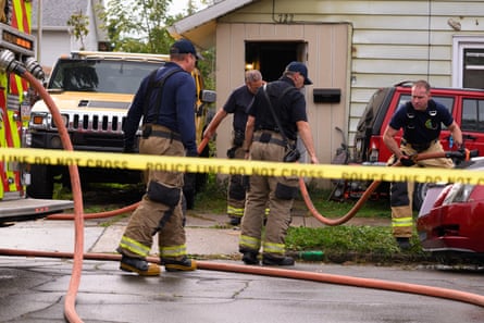 firefighters stand on street and clean outside of home with firehose