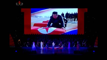 Performers stand on stage as North Korean leader Kim Jong-un is shown on a screen resting his hands on the coffins of soldiers repatriated after apparently being killed in Ukraine.