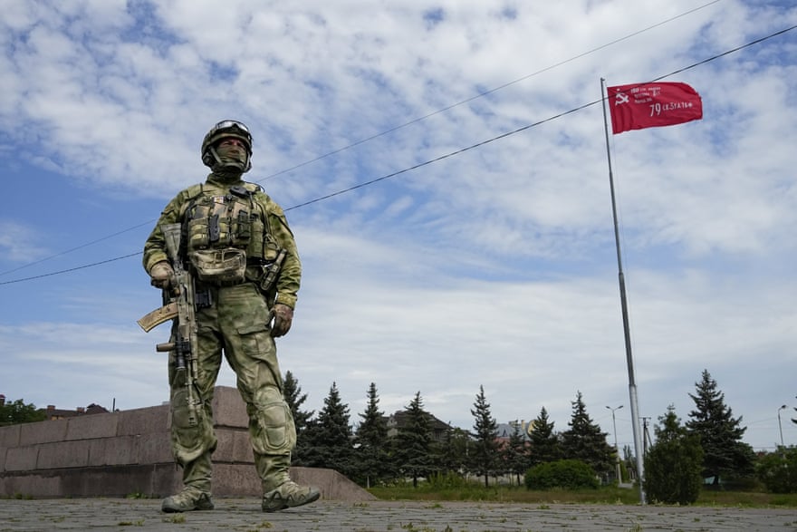 A Russian soldier guards an area in Kherson as a replica of the victory banner marking the 77th anniversary of the end of the second world war flies in the background.