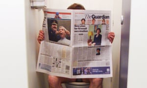 A man sitting on the toilet with his trousers down reading a copy of the broadsheet Guardian.