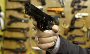 A man holds an Airsoft plastic BB gun in front of a shop display of the hobbyist replica firearms.