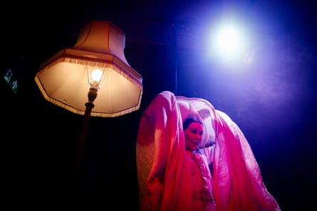 Kirsty Mann raises a sheet over her head, standing next to a standard lamp in Corpse.
