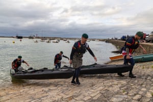 Four kayakers from the Royal Marines carry kayaks up to the shore