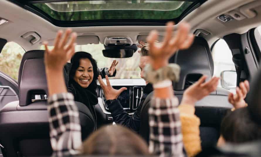 Famille joyeuse levant les mains tout en profitant d'un voyage en voiture électrique.