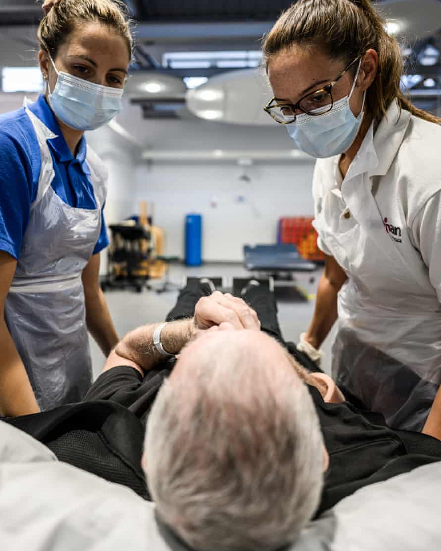 Two health workers standing over Geoff
