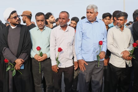 Men hold red roses at a funeral