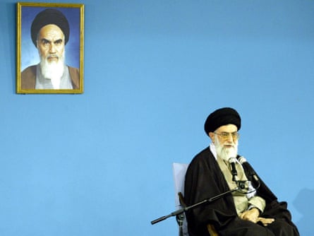 Khamenei speaking at a public meeting in Tehran, 2004, in fron t of a photograph of Ihis predecessor, Ayatollah Khomeini.