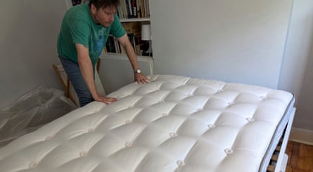 Man presses down to test firmness of a double mattress in a bedroom.