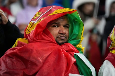 A Portugal fan shields himself from the rain with a flag during a storm before the Nations League semi-final against Germany.