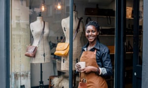 A small business owner looks to camera outside her handbag shop.